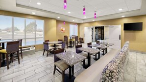 A hotel dining area with multiple tables and chairs, large windows, and a television on the wall.
