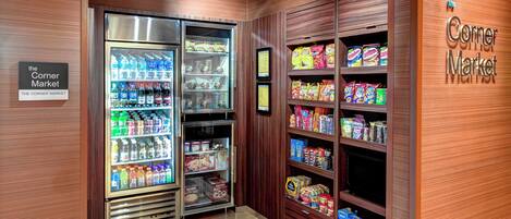 A corner market with refrigerated beverage dispensers and shelves stocked with snacks and cereals.