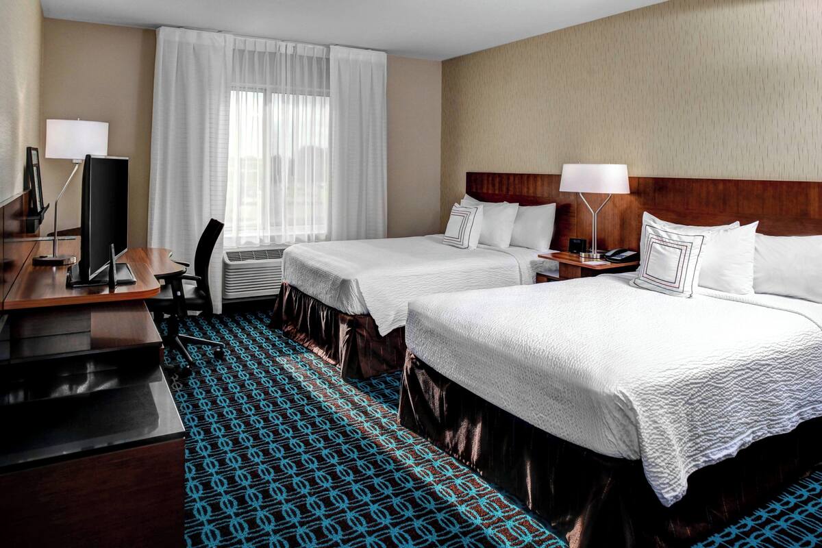 A hotel room with two beds, a desk, a chair, a TV, and a window with curtains.