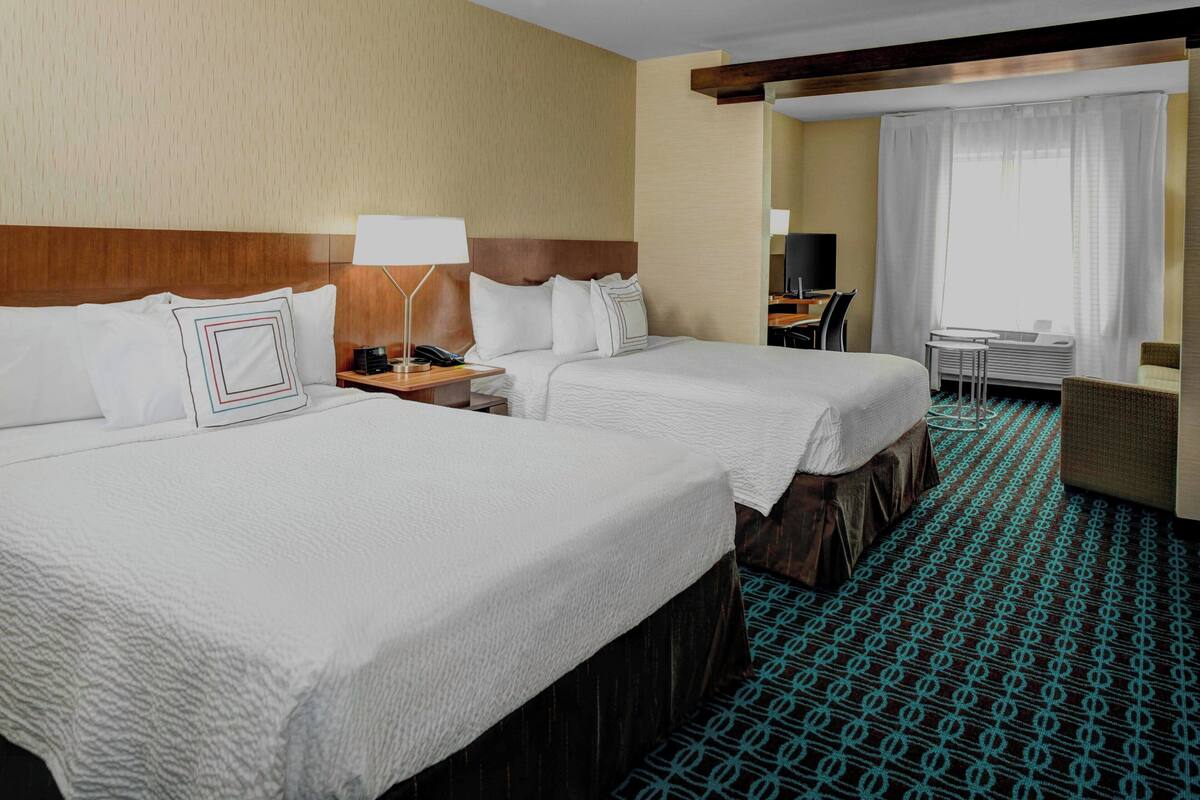 A hotel room with two beds, a desk, a chair, a TV, and a window with curtains.