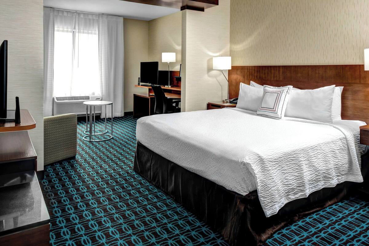 A hotel room with a large bed, a desk, a chair, a TV, and a window with curtains.