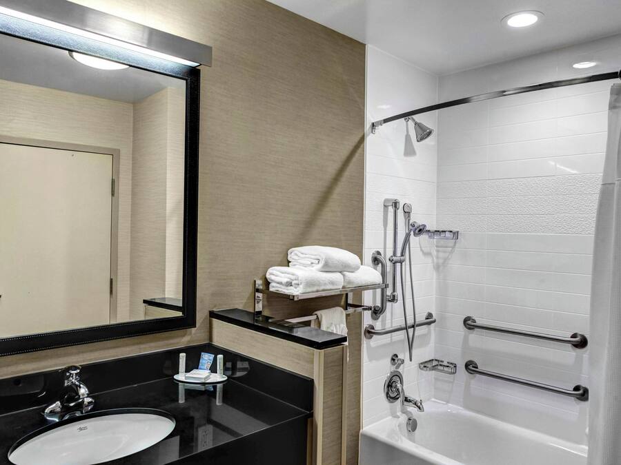 A modern bathroom with a black sink, a large mirror, a white bathtub, and a shower with grab bars.
