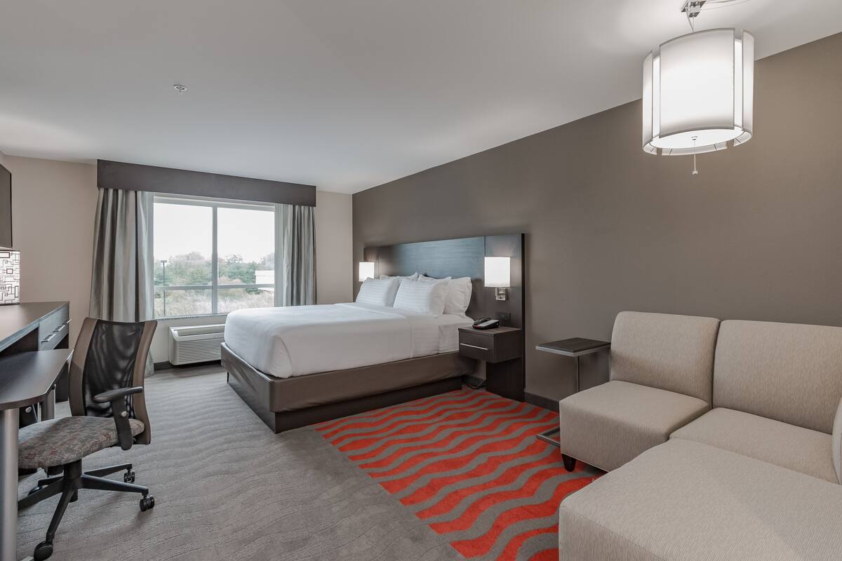Ein Hotelzimmer mit Bett, Schreibtisch, Stuhl, Sofa und einem großen Fenster.