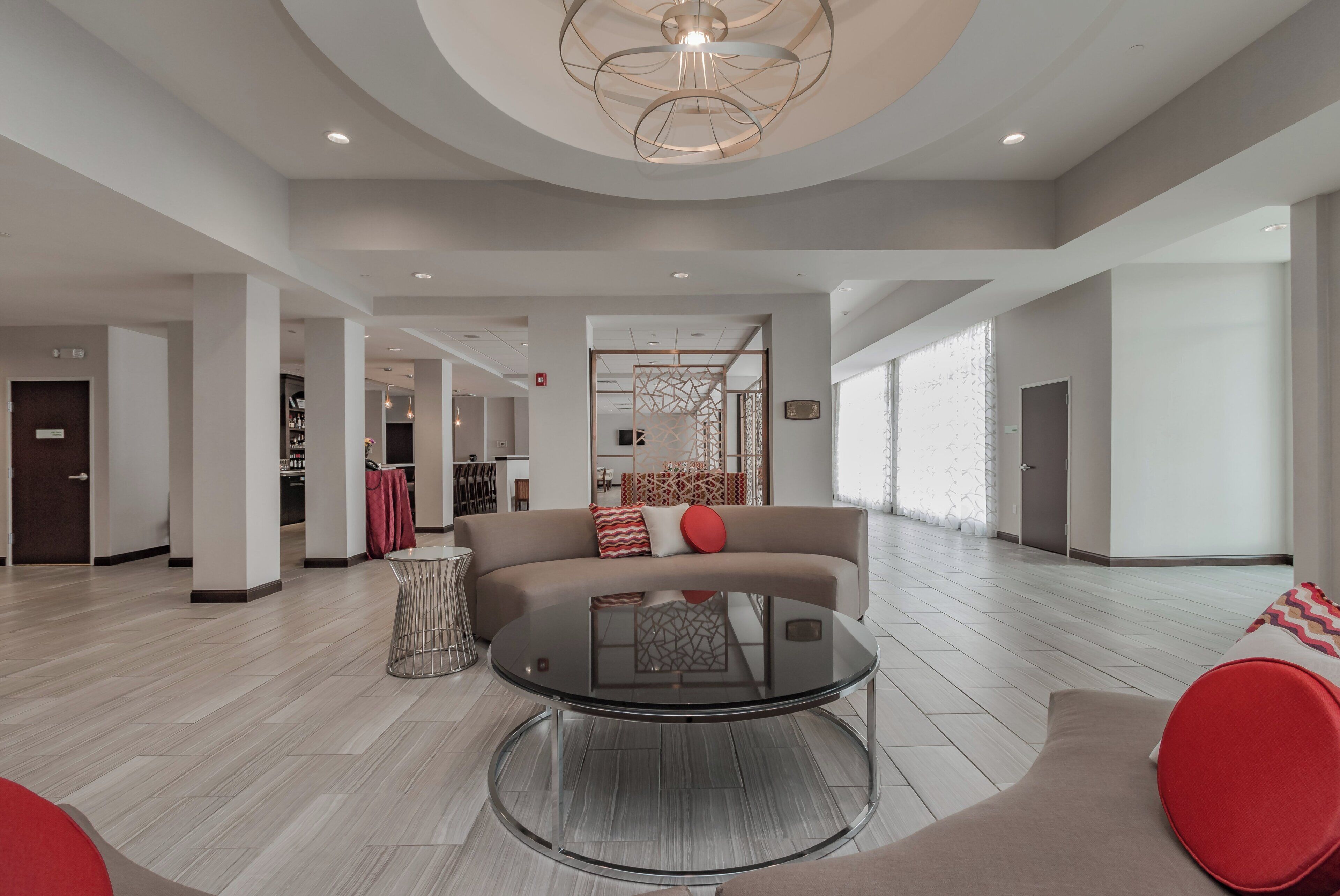 A spacious living area with a round glass coffee table, a sofa with red cushions, and a modern ceiling light fixture.