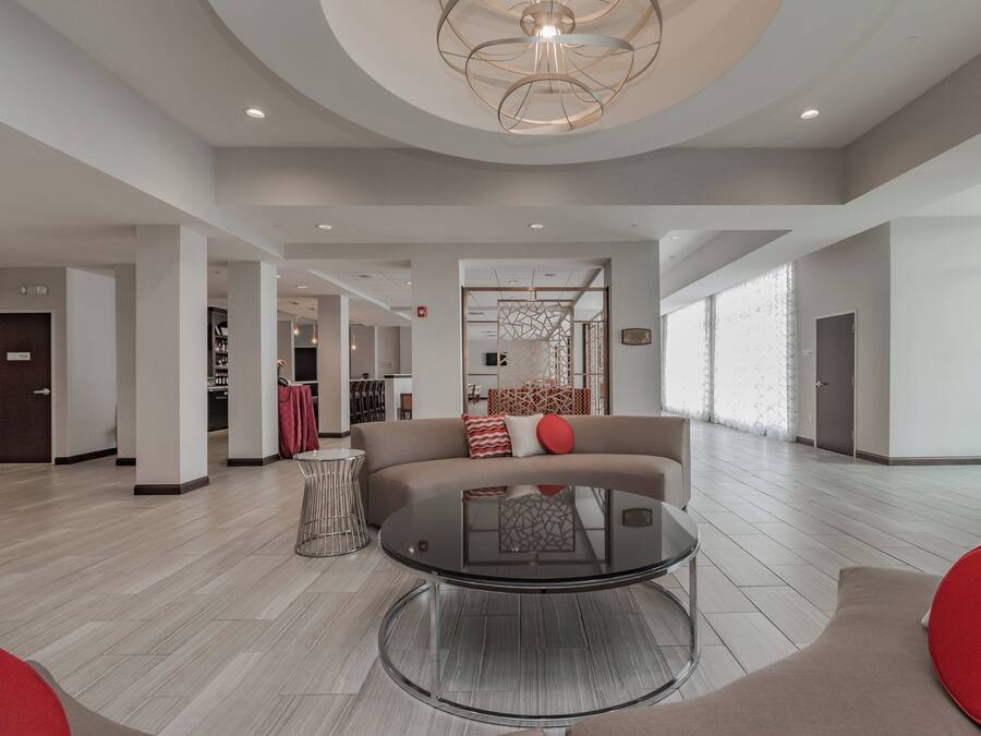 A spacious living area with a round glass coffee table, a sofa with red cushions, and a modern ceiling light fixture.