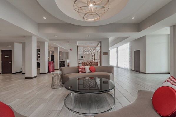 A spacious living area with a round glass coffee table, a sofa with red cushions, and a modern ceiling light fixture.