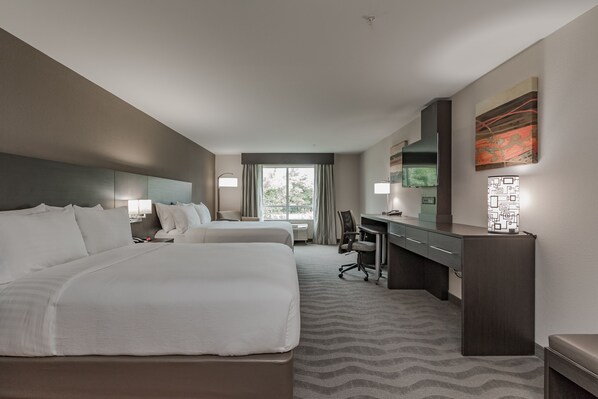 Une chambre d’hôtel avec deux lits, un bureau, une chaise, une lampe et une grande fenêtre.