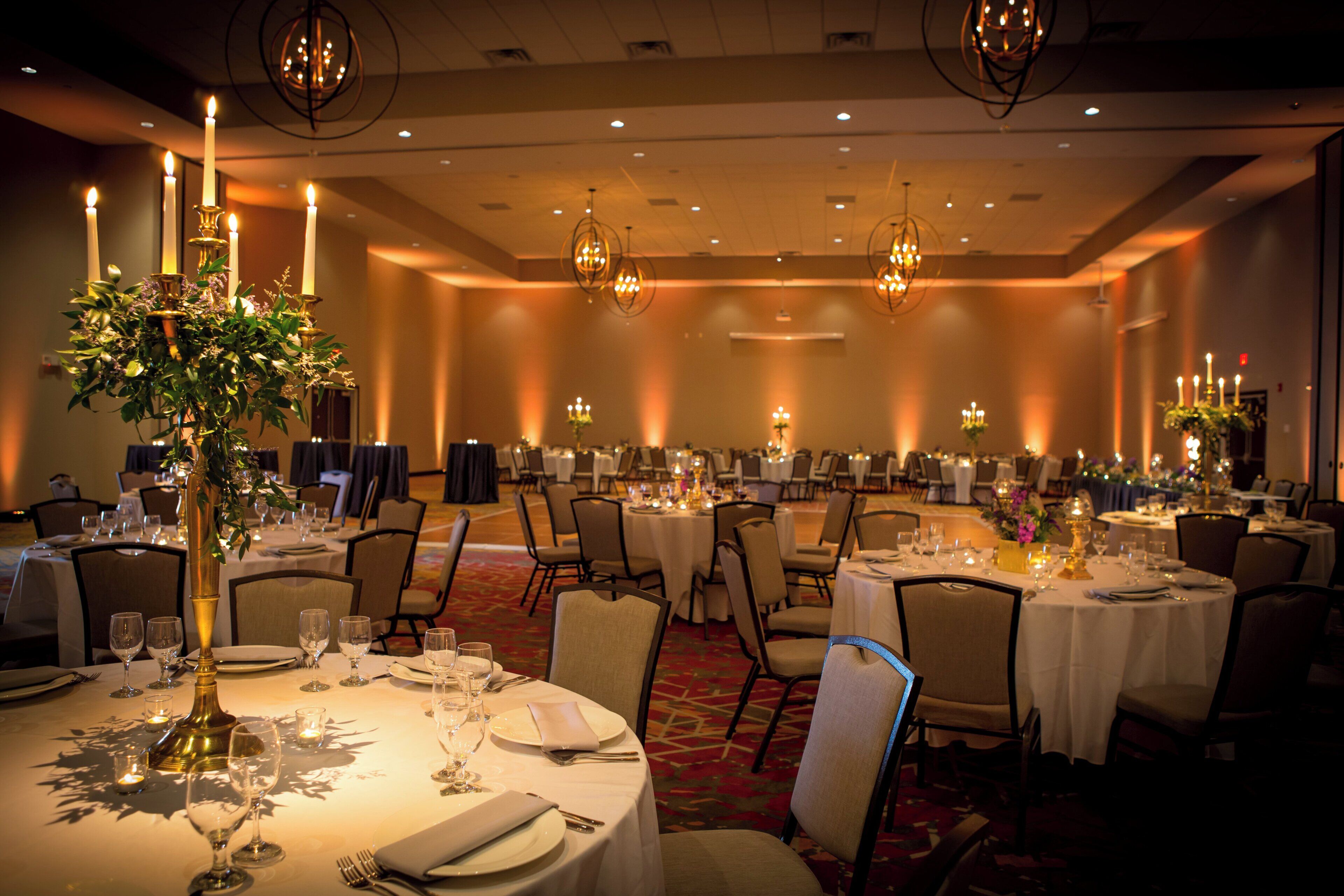 Un salón de banquetes con mesas redondas dispuestas para cenar, candelabros y centros de mesa con velas.