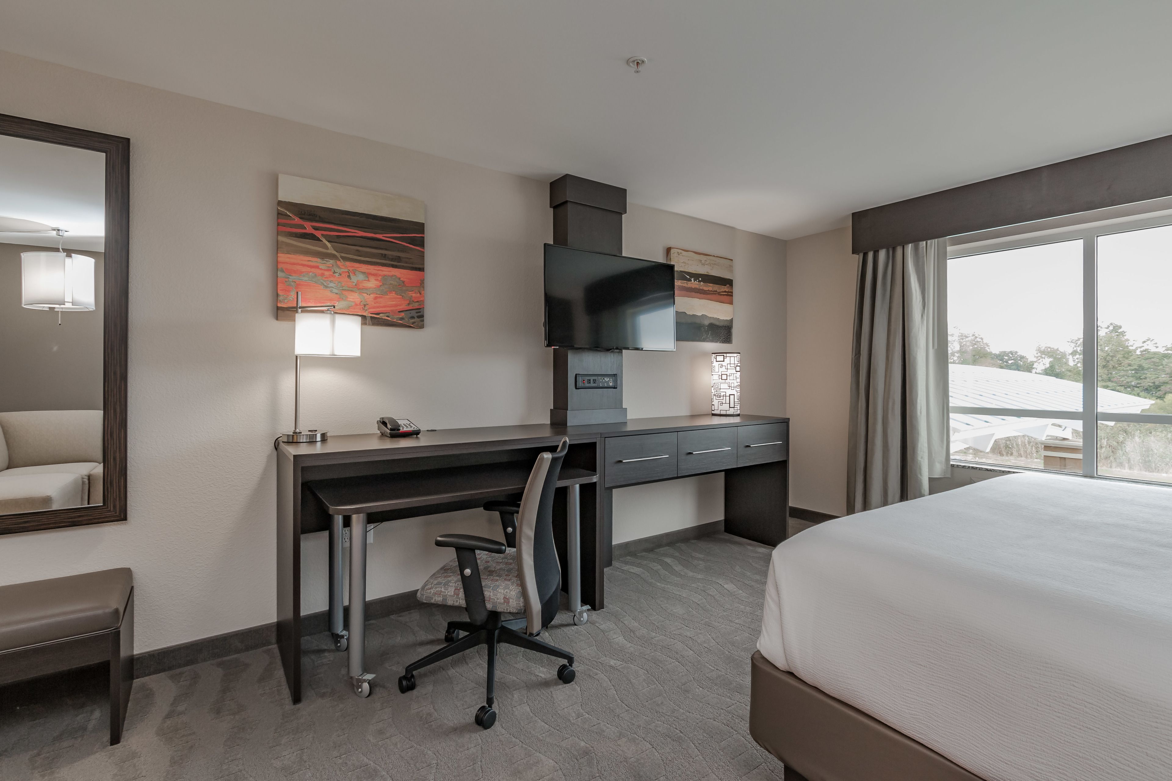 A hotel room with a bed, desk, chair, and large window.