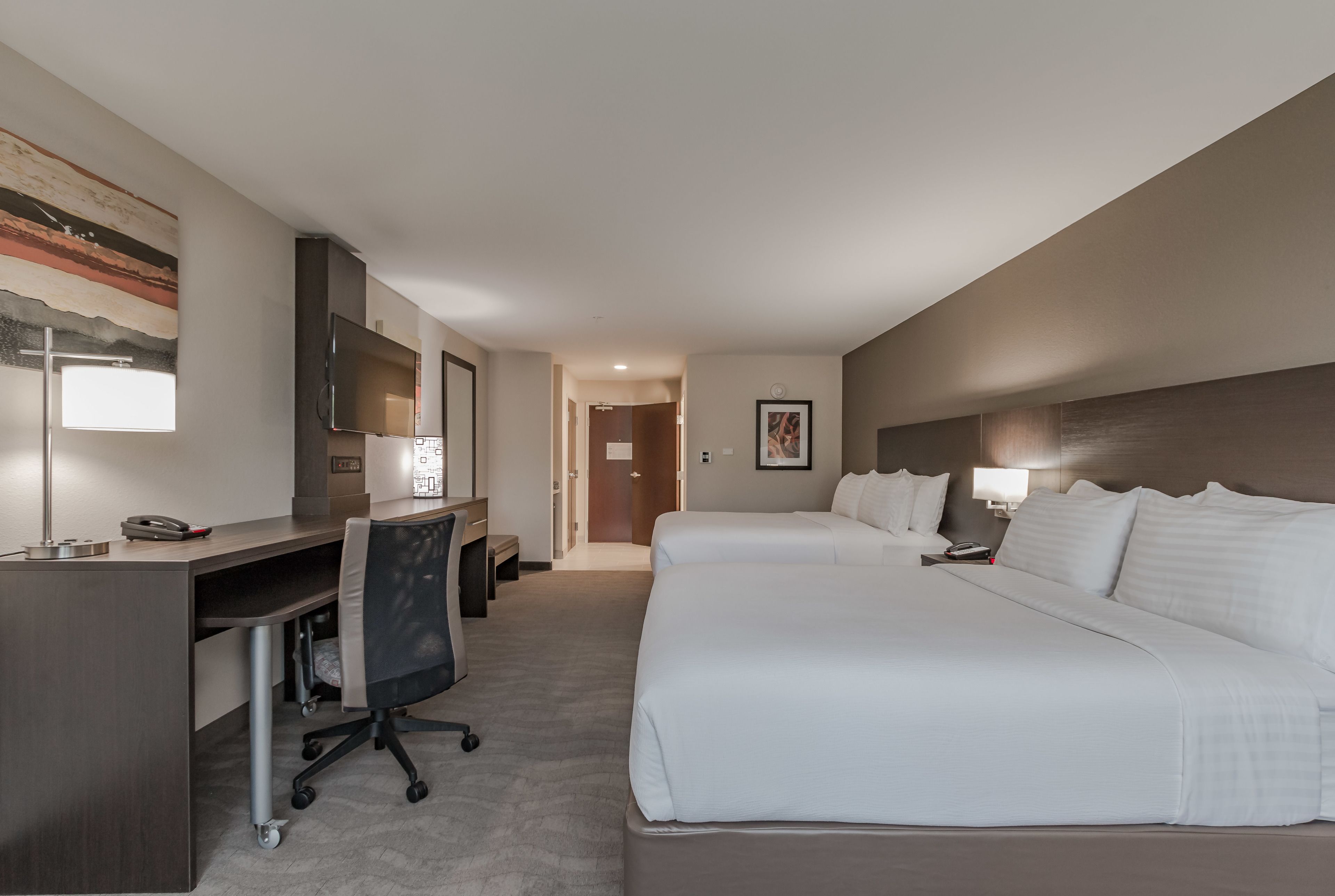 Une chambre d’hôtel avec un bureau, deux lits, une télévision et un tableau au mur.