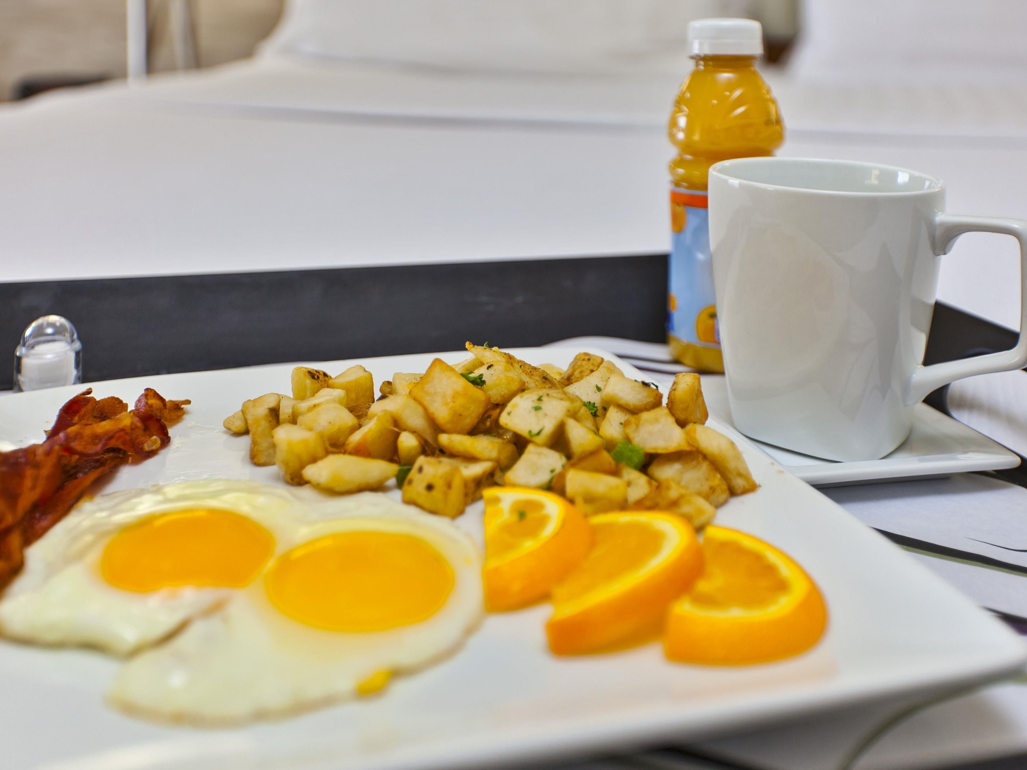 Un plato de desayuno con huevos, tocino, papas y rodajas de naranja.