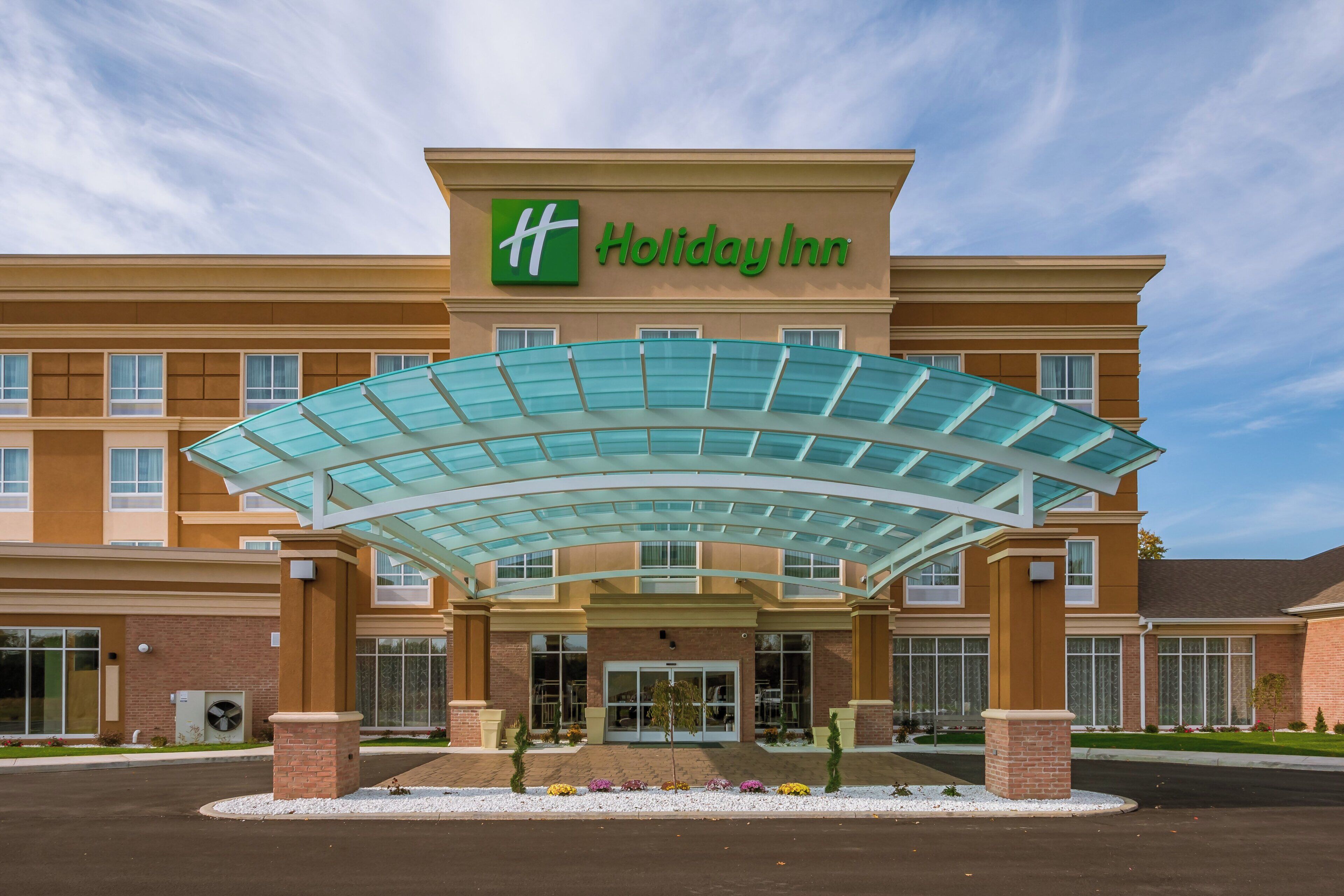 Entrada de um hotel Holiday Inn, com toldo de vidro e fachada de tijolos.