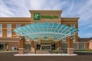 A Holiday Inn hotel entrance with a glass canopy and a brick facade.