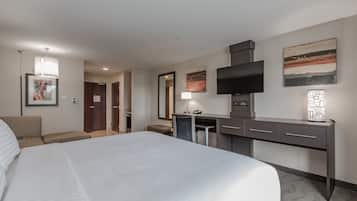Una habitación de hotel con una cama grande, un escritorio con televisor de pantalla plana, una silla, una lámpara de escritorio y obras de arte en las paredes.