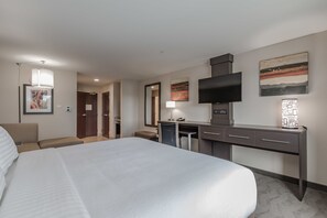 Une chambre d’hôtel dotée d’un grand lit, d’un bureau avec un téléviseur à écran plat, d’une chaise, d’une lampe de bureau et d’œuvres d’art accrochées aux murs.