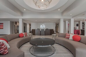 A spacious lobby with a central round table, sofas with red cushions, and a reception desk.