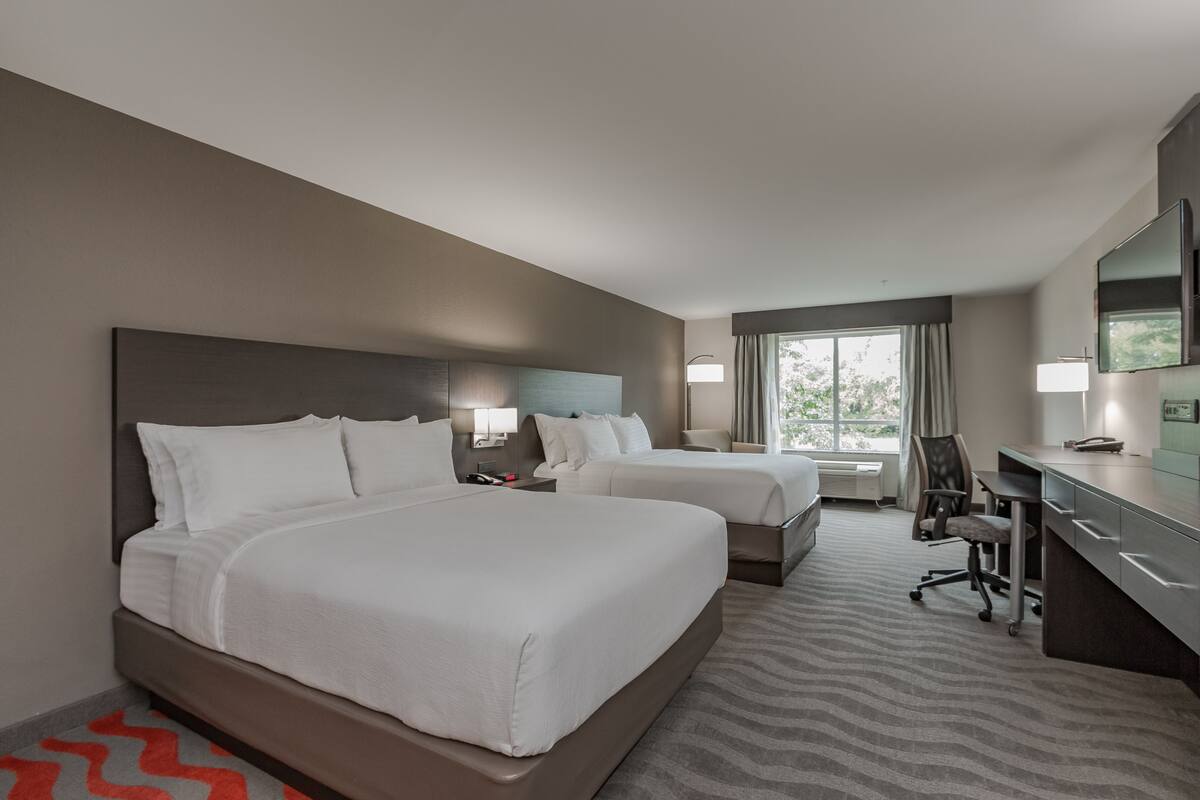 Ein Hotelzimmer mit zwei Betten, einem Schreibtisch, einem Stuhl und einem großen Fenster.