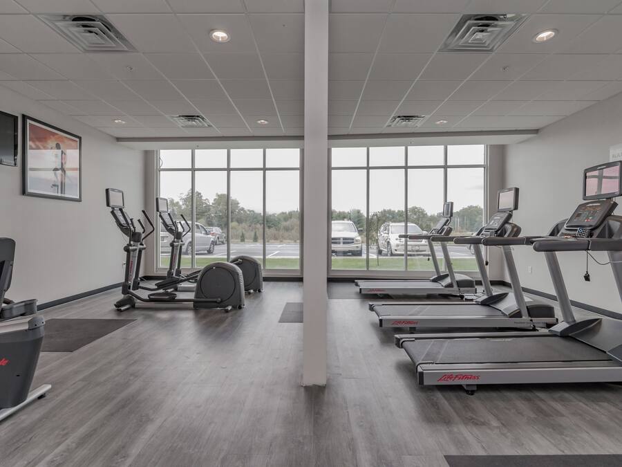 A gym with treadmills, elliptical machines, and a stationary bike, large windows, and a view of the parking lot.