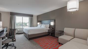 A hotel room with a bed, a desk, a chair, a sofa, a red patterned rug, and a large window.
