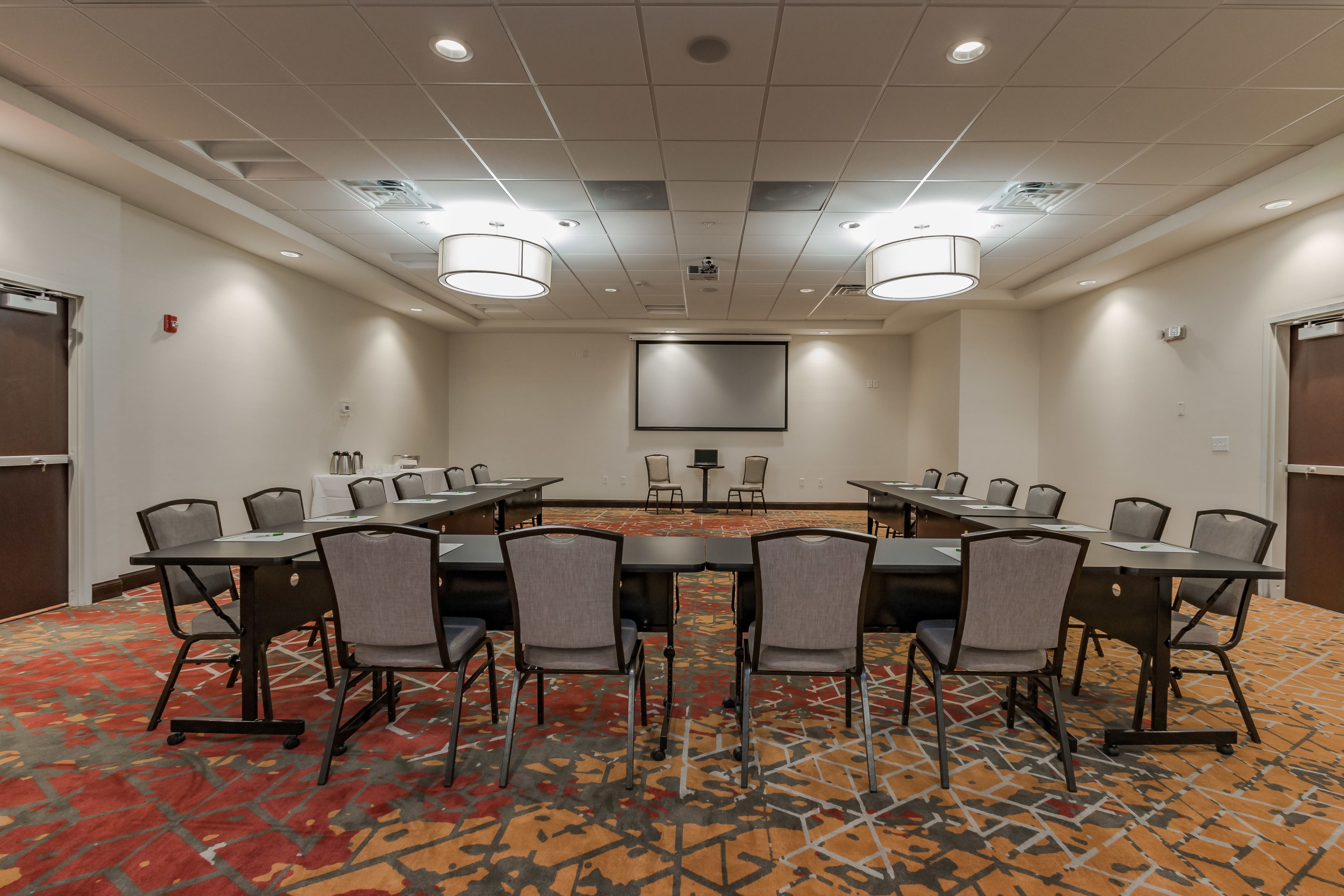 A conference room with a large table, multiple chairs, a projector screen, and a carpeted floor.