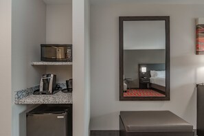 Une chambre d’hôtel compacte comprenant un coin cuisine, un lit, un miroir et un petit espace salon.