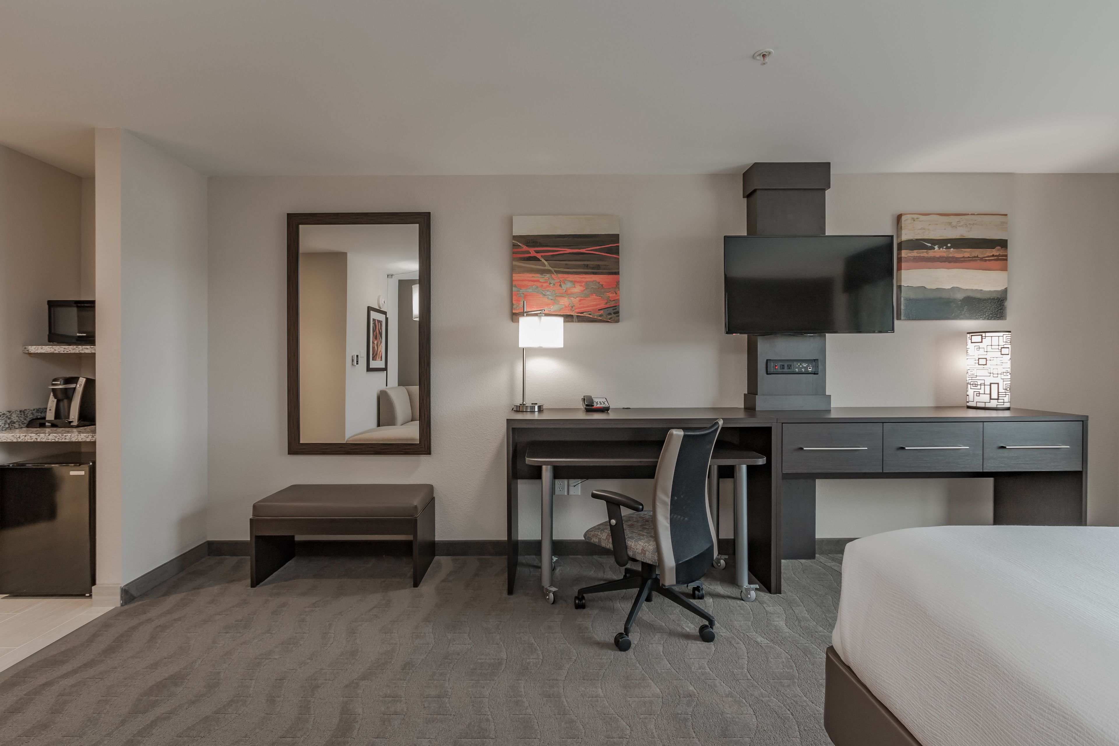 A hotel room with a bed, desk, chair, and a small bench.