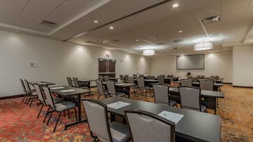 A conference room with multiple tables and chairs, a projector screen, and a carpeted floor.
