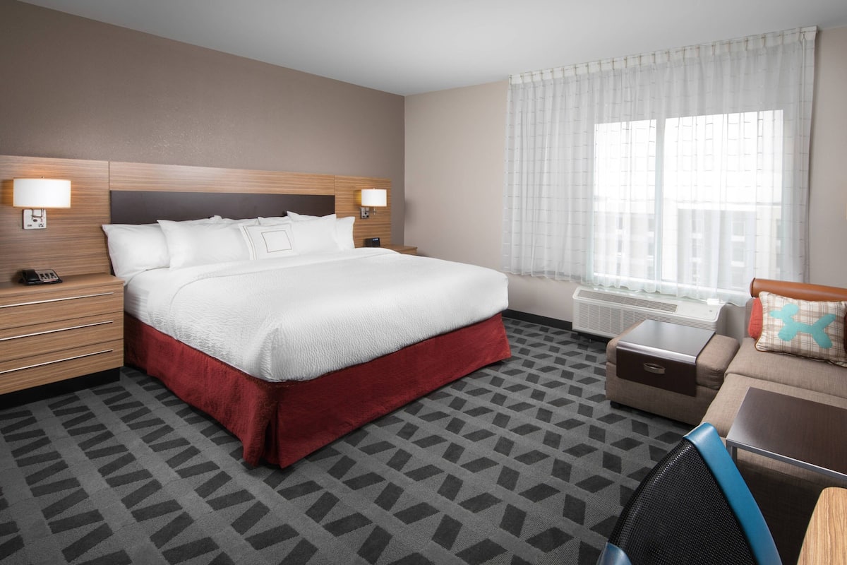 Ein Hotelzimmer mit einem großen Bett, einer Schlafcouch, einem Schreibtisch und einem Fenster mit Vorhängen.