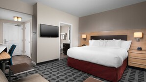 Une chambre d’hôtel avec un grand lit, un bureau, une chaise, une télévision et une salle de bain visible à travers une porte ouverte.
