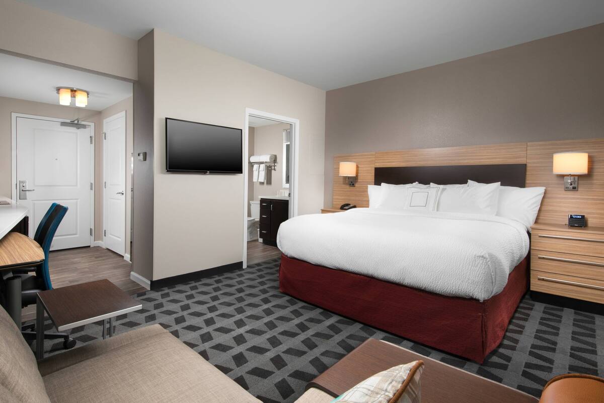 Ein Hotelzimmer mit einem großen Bett, einem Schreibtisch, einem Sessel, einem Fernseher und einem sichtbaren Badezimmer durch eine offene Tür.