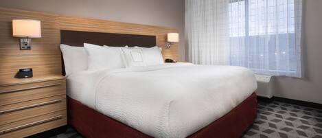 Ein Hotelzimmer mit einem großen Bett, einem Holzkopfteil, zwei Nachttischen mit Lampen, einem Telefon und einem Fenster mit durchsichtigen Vorhängen.