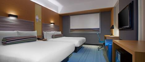 A hotel room with two beds, a desk, a TV, and a window with blinds.