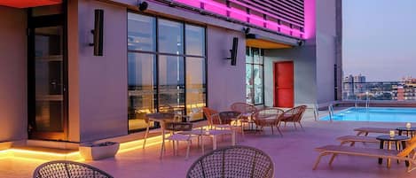 A modern hotel exterior with outdoor seating and a pool.