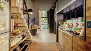 A modern kitchen area with a wooden counter displaying various food items and a staircase with a glass railing leading to an upper level. - Aloft by Marriott Asuncion (Asunción)
