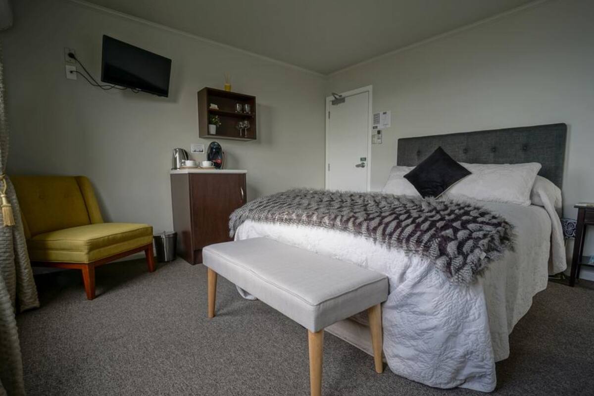 A bedroom with a bed, a bench, a chair, a TV, a cabinet, and a door.