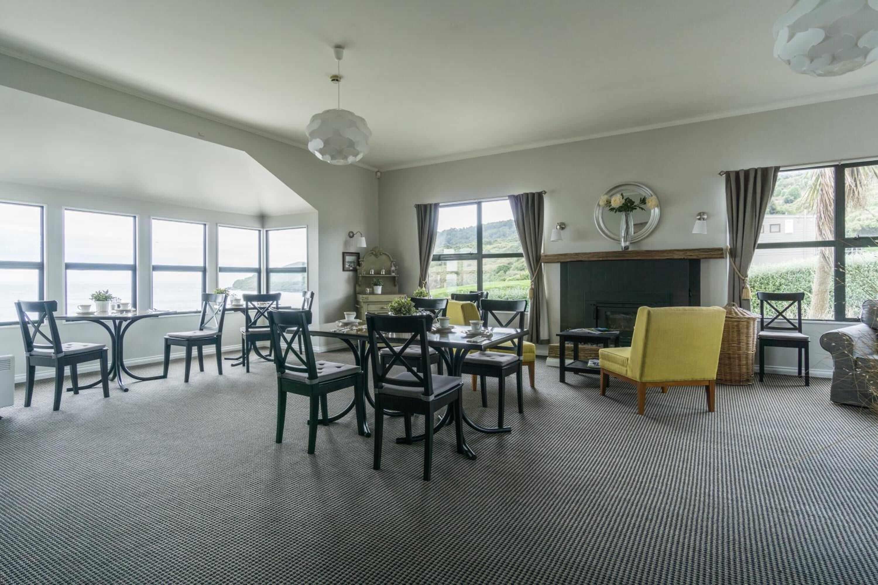 A spacious room with large windows, a fireplace, and a dining area with chairs and tables.