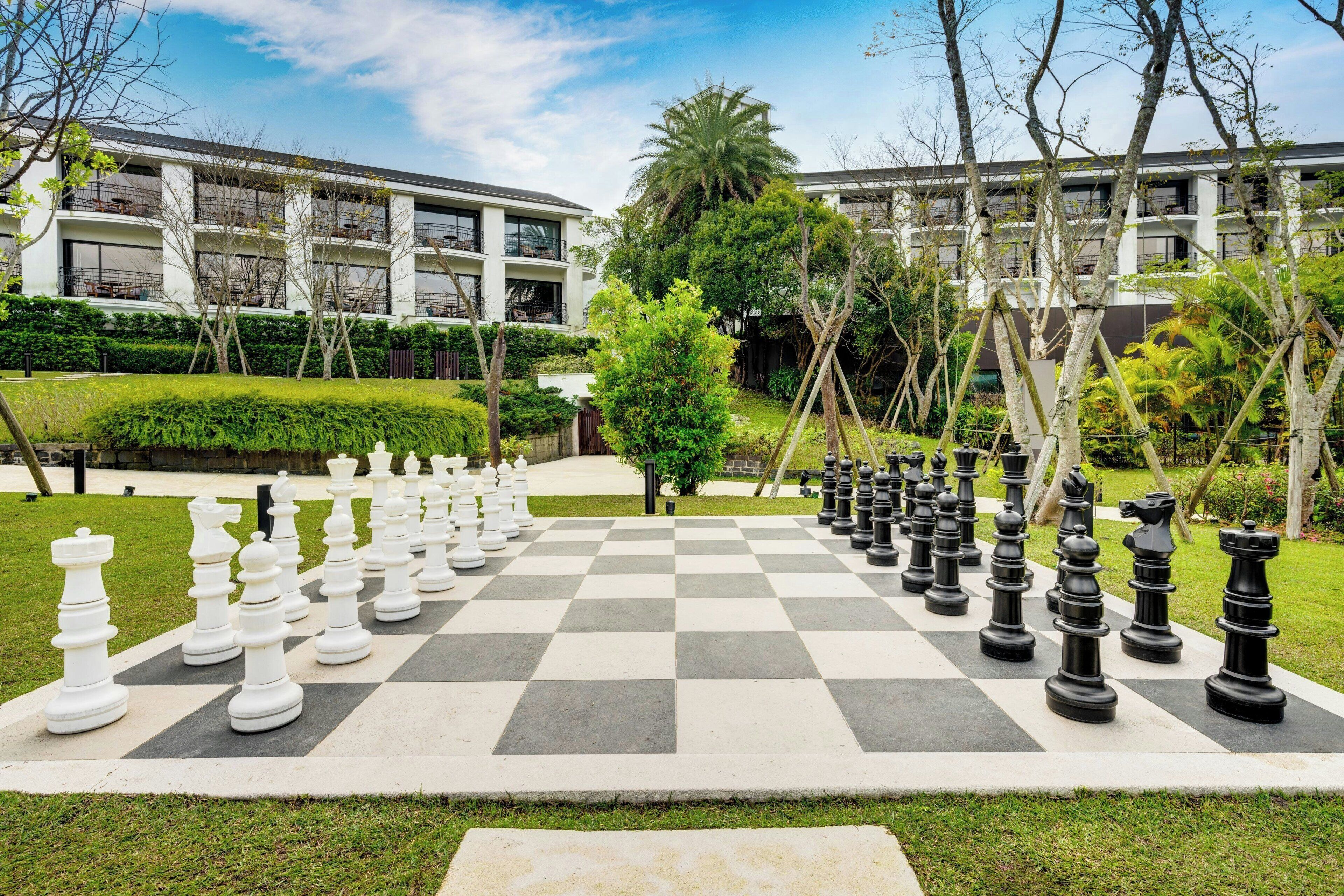A large outdoor chessboard set up in a courtyard with modern buildings in the background.