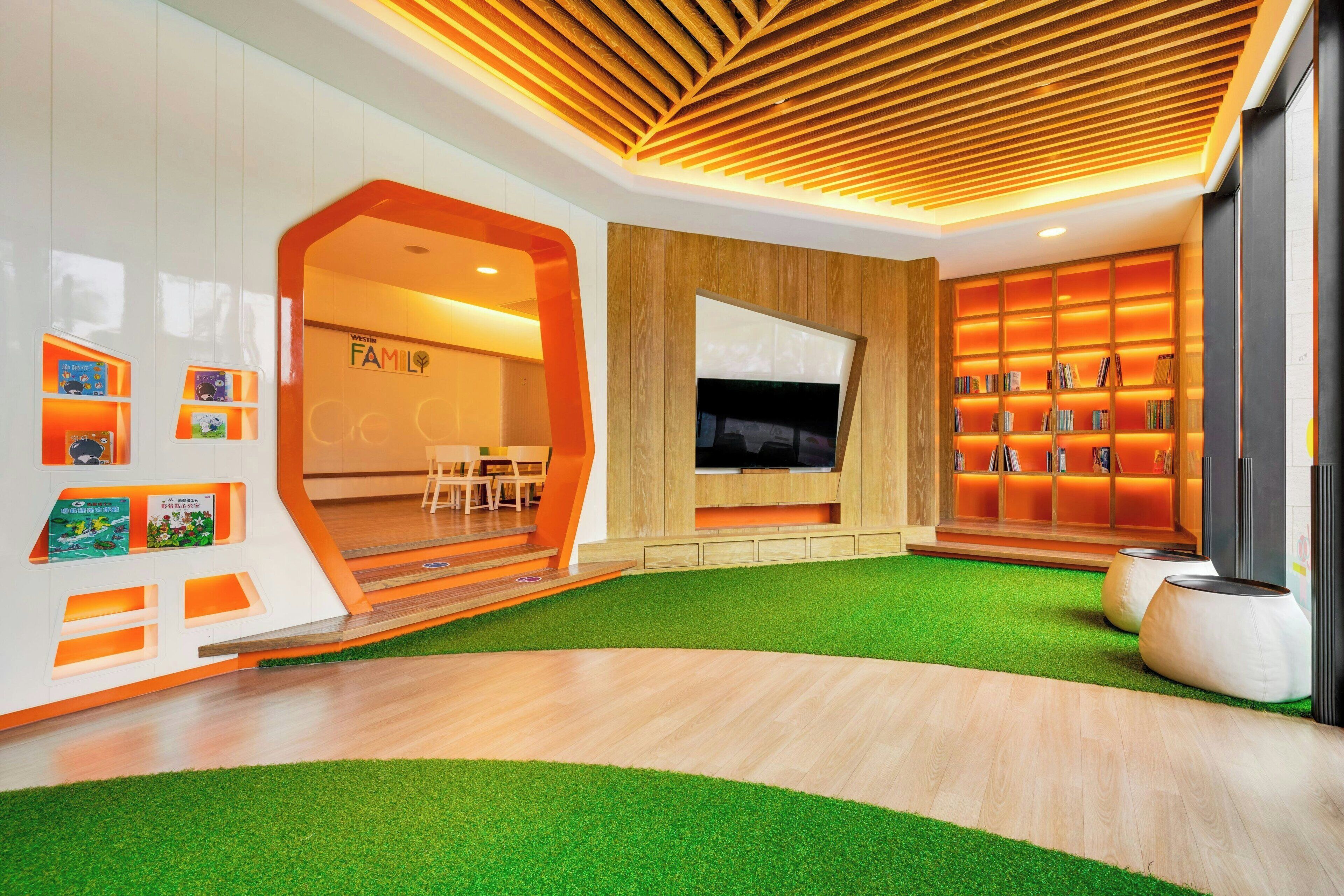 A modern living room with a wooden ceiling, a flat-screen TV, a bookshelf, and a green artificial turf area.