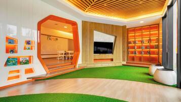 A modern living room with a wooden ceiling, a flat-screen TV, a bookshelf, and a green artificial turf area.