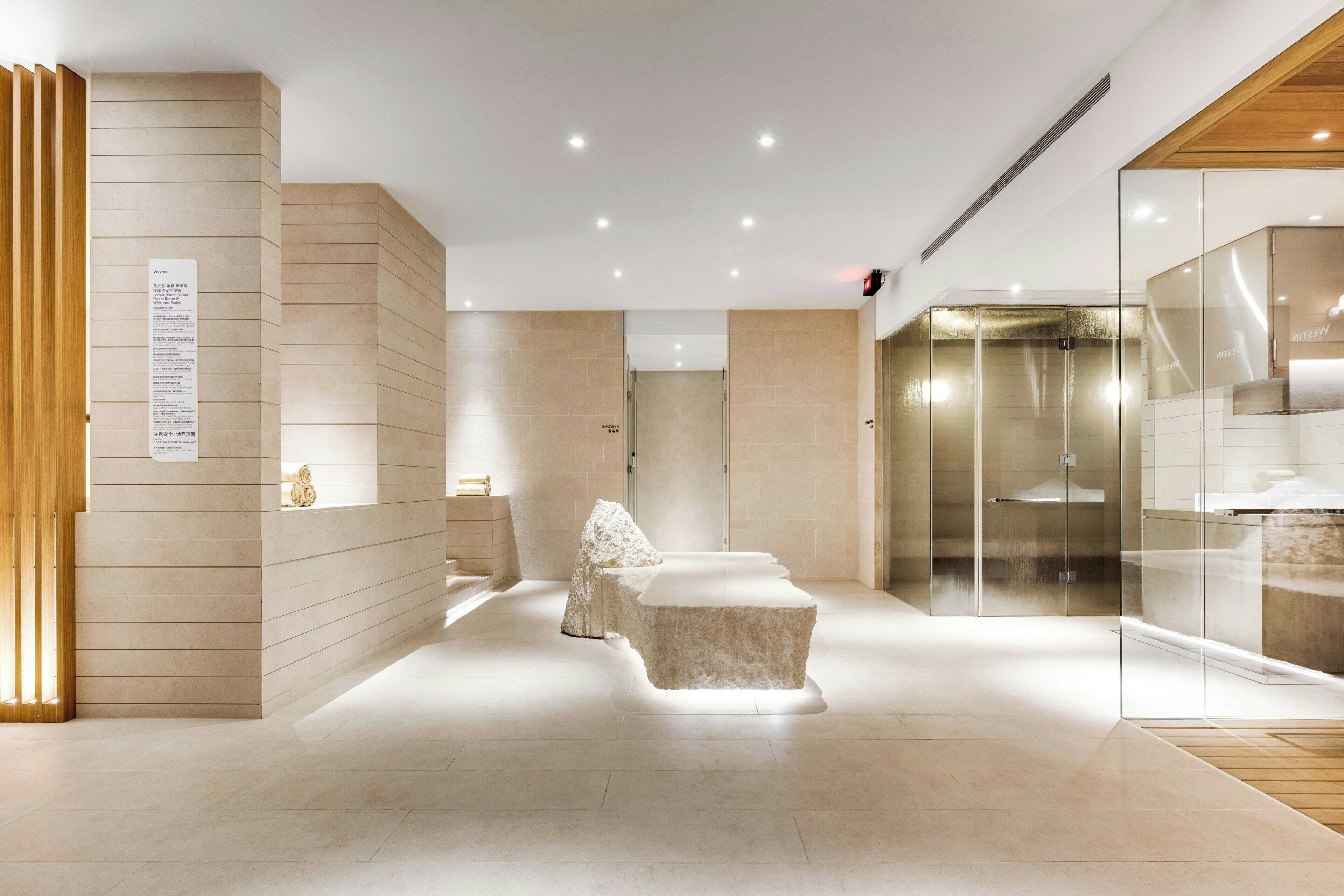 A modern hotel lobby with a minimalist design, featuring a reception desk, a seating area with a unique rock-like structure, and a glass-enclosed shower area.