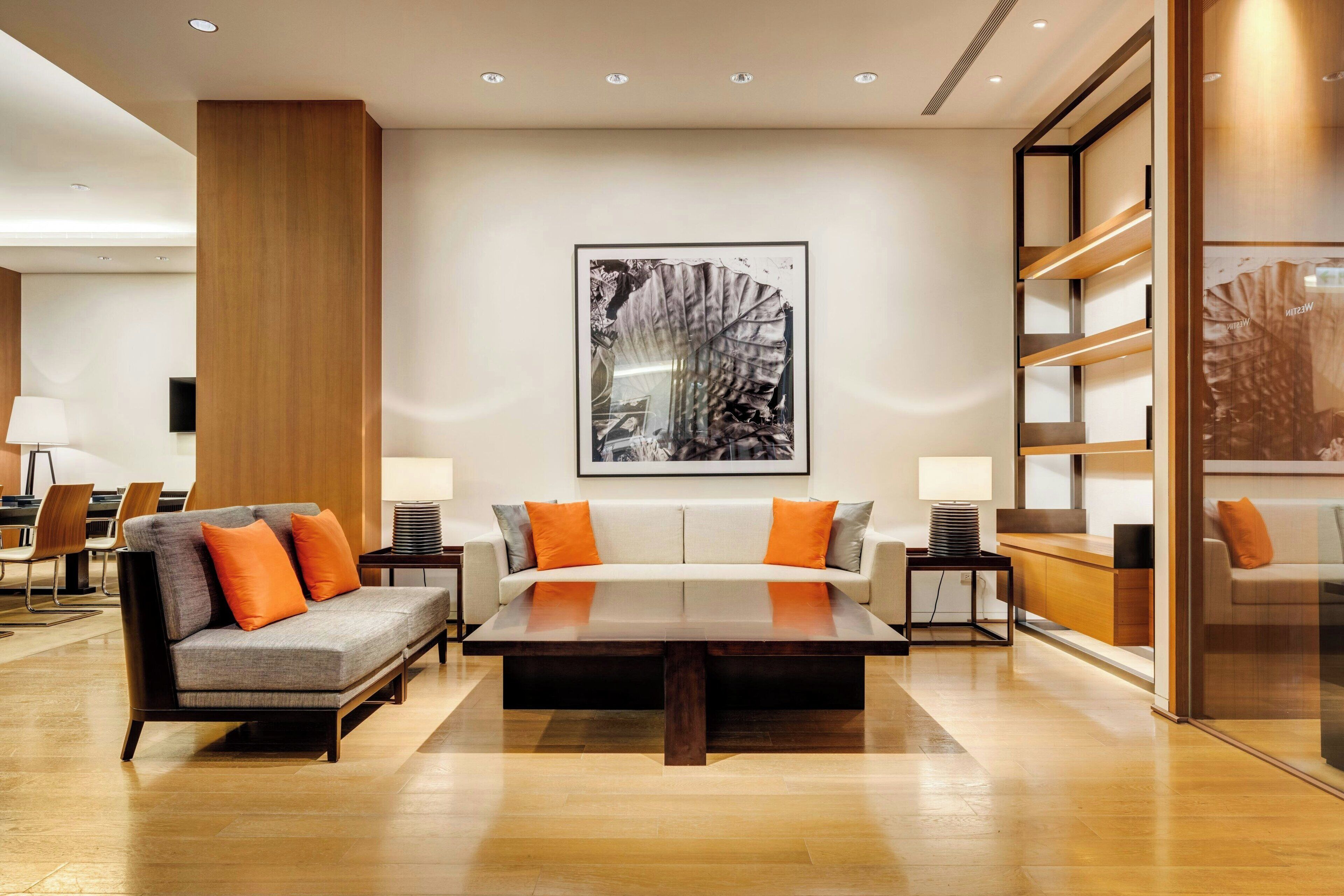 A modern hotel lobby with a central seating area, a large framed artwork on the wall, and a glass partition on the right.