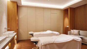 A modern spa room with two treatment beds, a sofa, and a vanity with sinks.