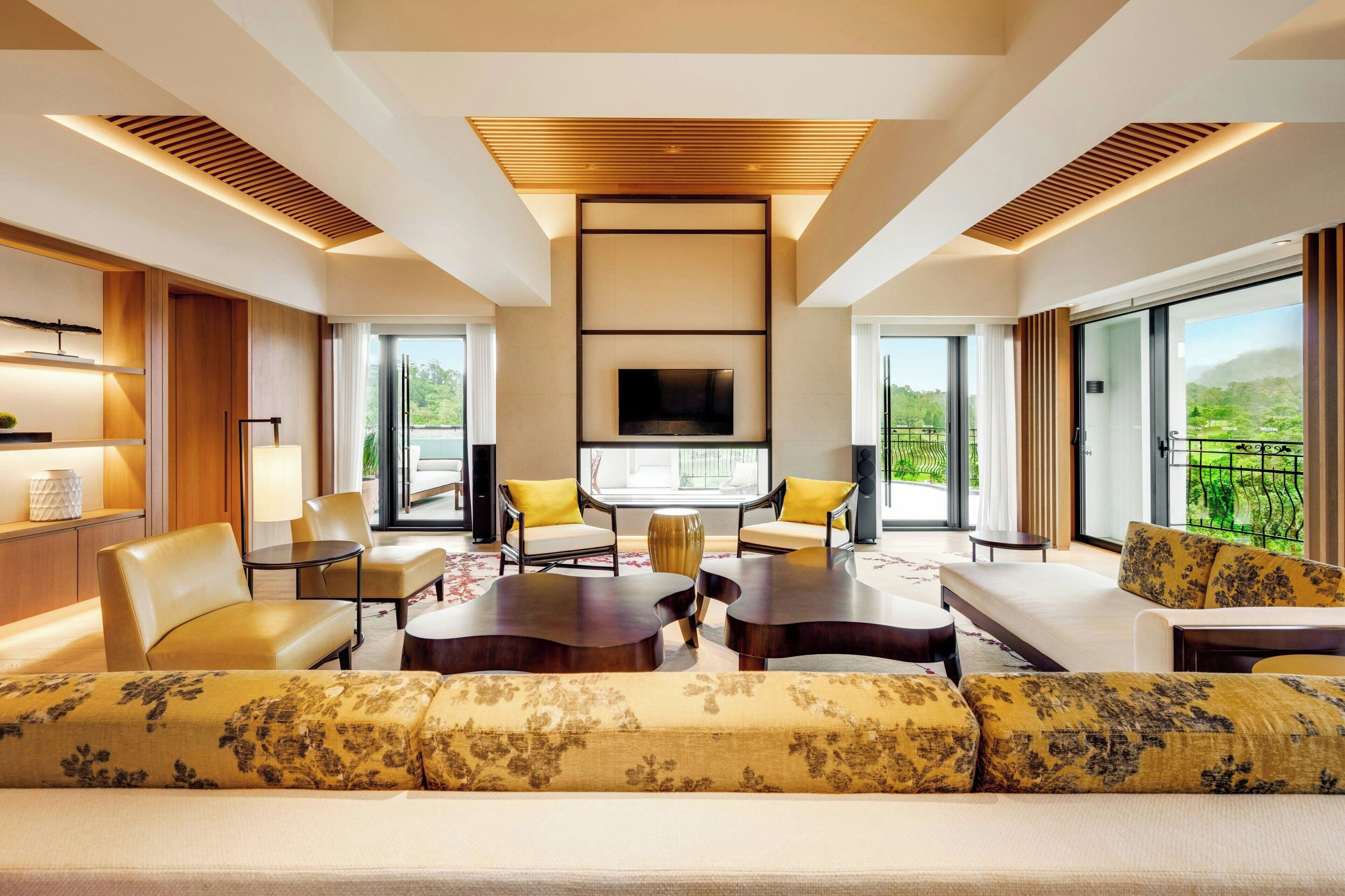 Habitación de hotel moderna con un sofá grande, dos sillones, una mesa de centro y un televisor de pantalla plana montado en la pared.