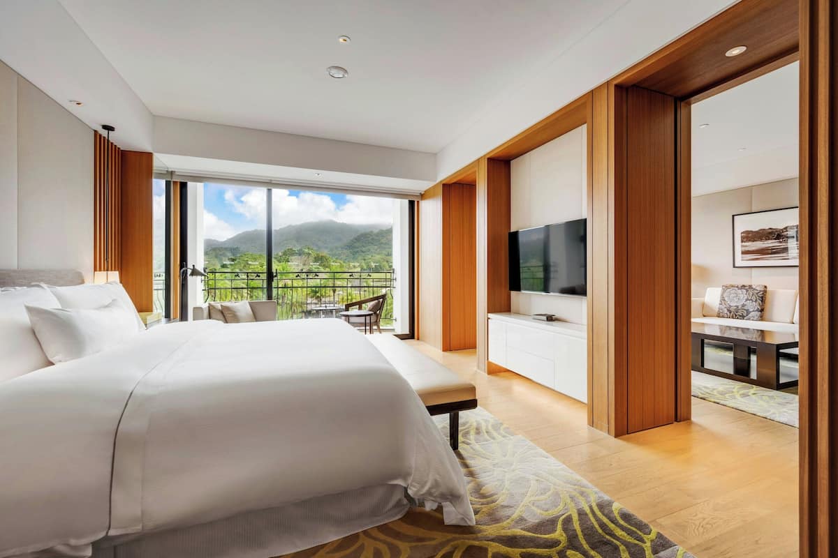 Ett modernt hotellrum med en stor säng, en TV, en balkong med utsikt över bergen och en matplats.
