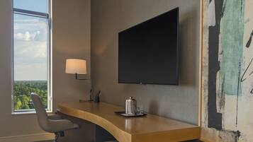 A modern office space with a curved desk, a chair, a mounted TV, and a window with a view of greenery.