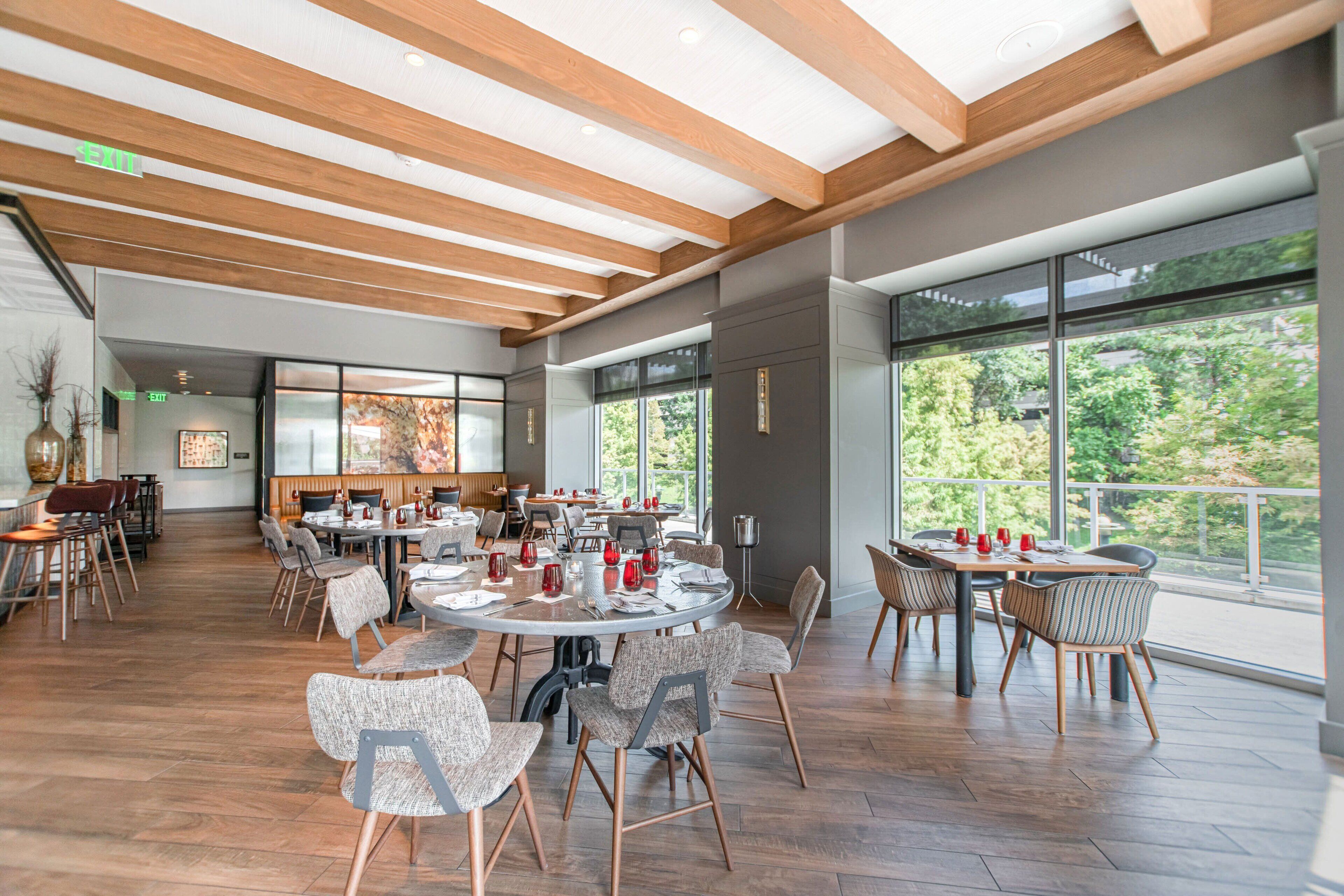 Un vaste espace dédié à la salle à manger, avec des tables et des chaises rondes, de grandes fenêtres offrant une vue sur la verdure et un design moderne au niveau du plafond.