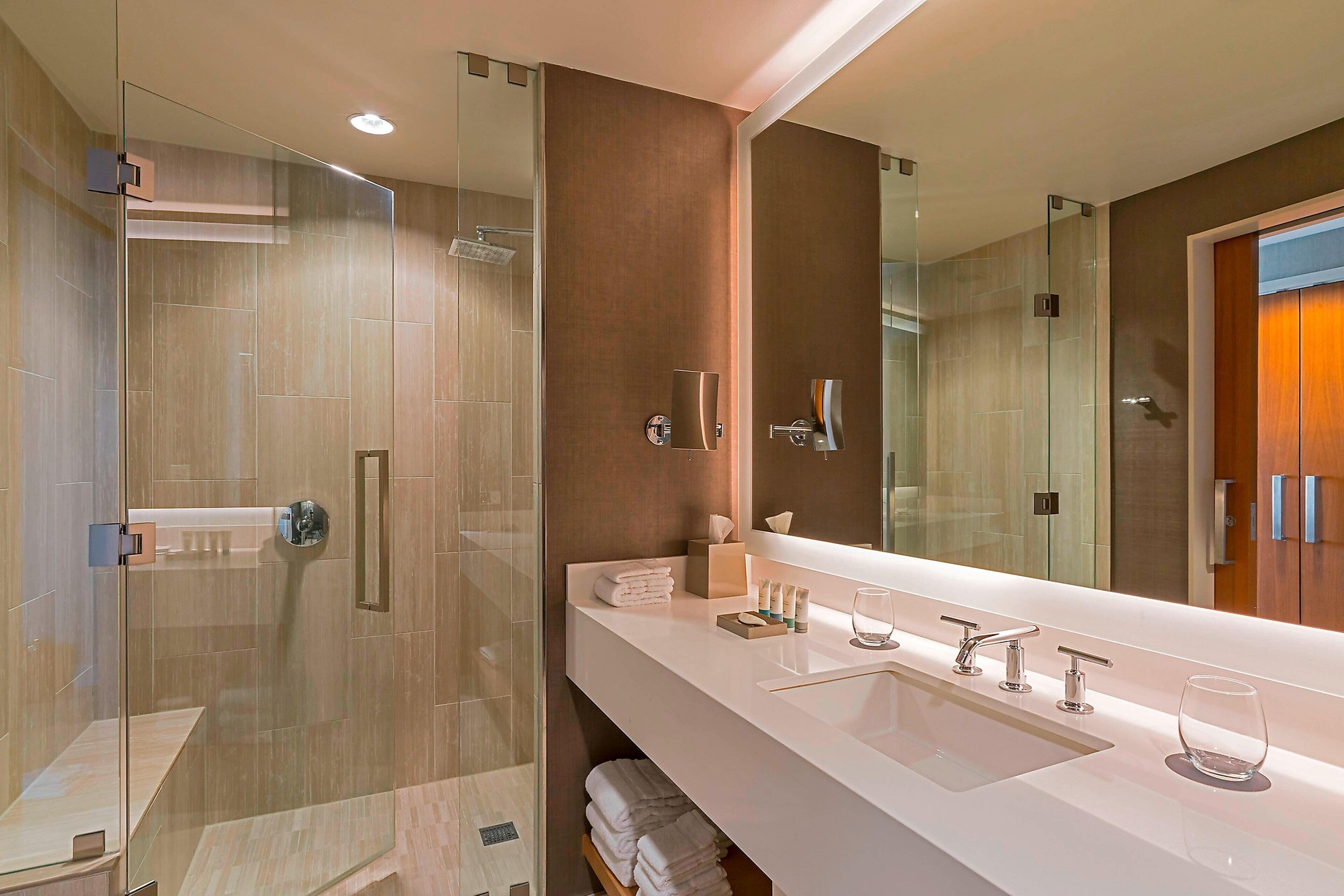 A modern bathroom with a glass-enclosed shower, a large mirror, and a white sink with multiple faucets.