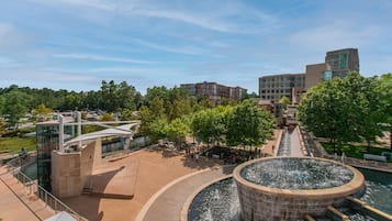 A modern building with a circular water feature in the center, surrounded by a plaza with benches and trees.