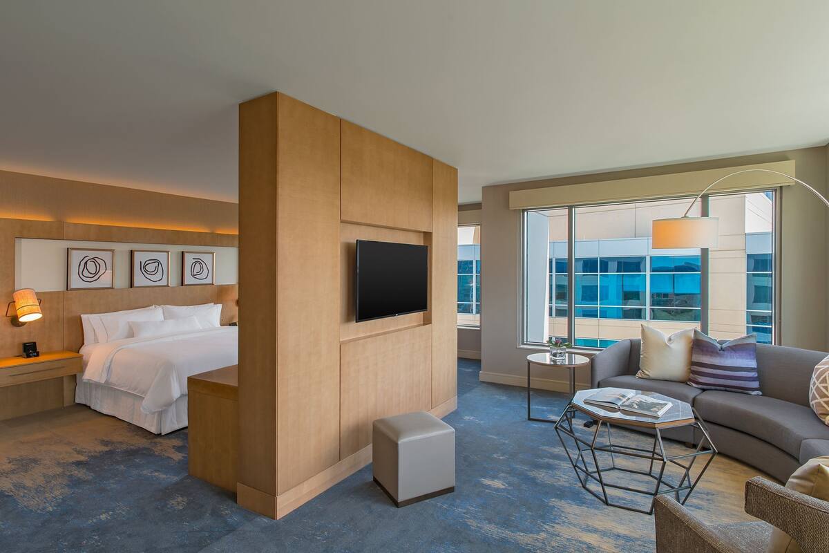 Una habitación de hotel moderna con cama, televisor, sofá y una mesita.