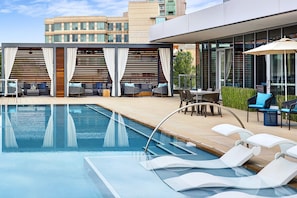 A modern outdoor pool area with lounge chairs, a table, and a covered seating area.